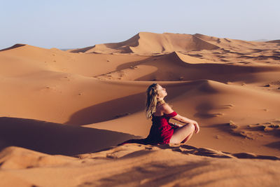 Side view of young woman sitting at desert