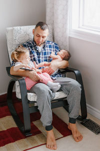 Friends holding daughters while sitting on chair at home
