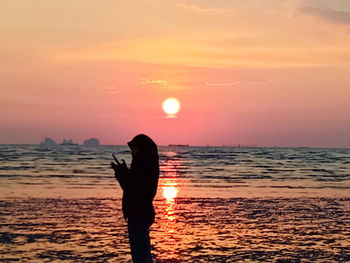 Silhouette man standing on beach against sky during sunset