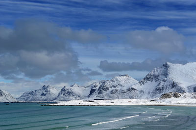 Scenic view of sea by snowcapped mountain against sky