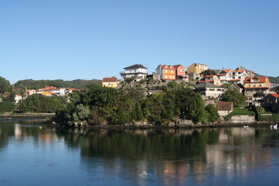 Houses and trees by buildings against clear blue sky