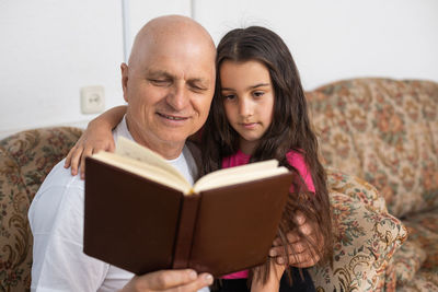 Man reading book with granddaughter at home