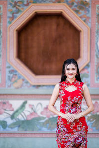 Portrait of a smiling young woman standing against built structure