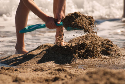 Low section of person digging on beach against sky