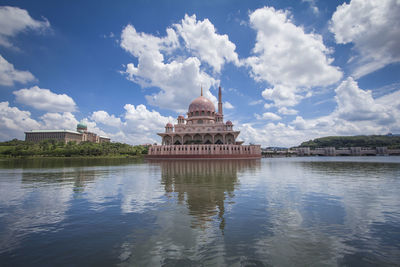 View of temple by lake against cloudy sky