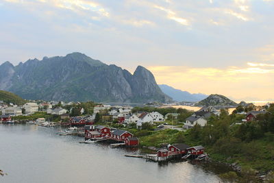 High angle view of houses by sea and mountains against cloudy sky