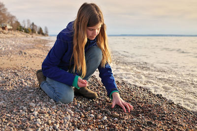 Young adolescent girl collects beautiful colorful rocks, pebbles and shells on the beach