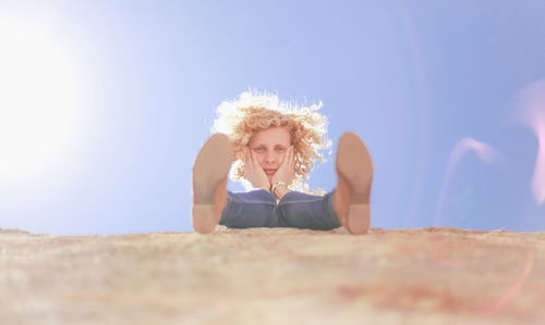 Portrait of thoughtful woman sitting on stone wall against sky