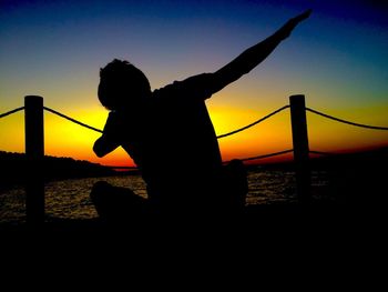 Silhouette of chainlink fence against sea at sunset