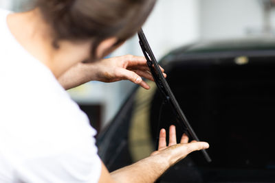 Rear view of man checking windshield wiper of car at garage