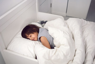 Child boy lies in a white children's bed with a blanket in a room with toys rabbits