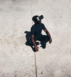 High angle view of teenage boy looking virtual reality simulator while sitting on street during sunny day