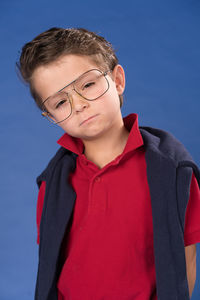 Portrait of cute boy wearing eyeglasses standing against blue background