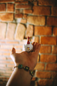 Close-up of hand holding object against brick wall