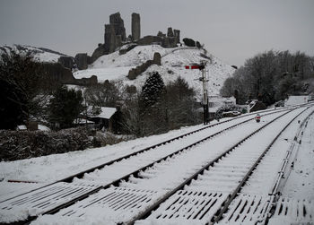 Snow covered railroad tracks by building against sky