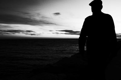 Silhouette man standing by sea against sky