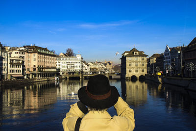 Rear view of man overlooking river against built structures