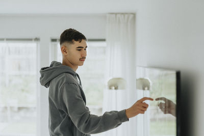 Side view of teenage boy touching smart tv screen in living room