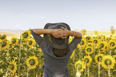 Rear view of woman standing by sunflower plants against sky