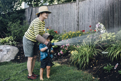 Happy grandmother with grandson watering plants together in garden