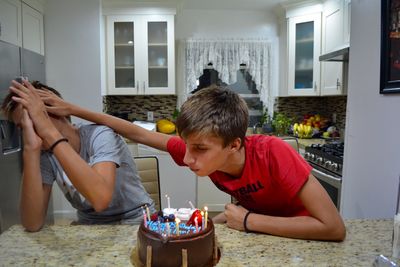 Teenage boy pushing brother while blowing candle during birthday