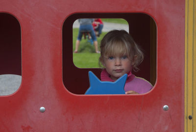 Portrait of cute girl looking through window at playground