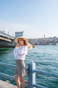 Portrait of young woman standing by railing against sky