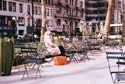 Woman sitting on table by bench in city