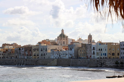 Buildings by sea against cloudy sky