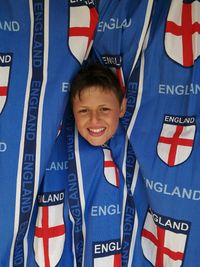 Portrait of happy teenage boy amidst blue curtains with english flag