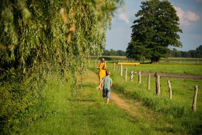 Rear view of woman and boys running on grassy field