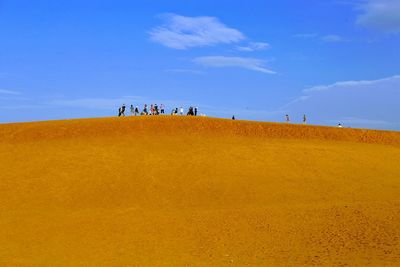 People on sand dune in desert against blue sky