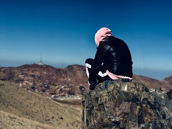 Rear view of man standing on rock formations against clear sky