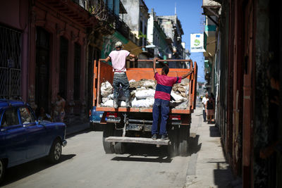 Rear view of men on garbage truck at city street