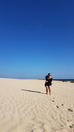 Young woman standing on sand against clear blue sky