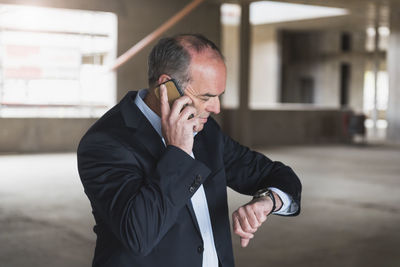 Businessman on cell phone in building under construction checking the time