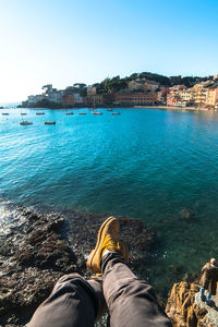 Low section of man sitting on rock by sea against clear sky