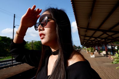 Close-up of woman shielding eyes while standing at railroad station platform