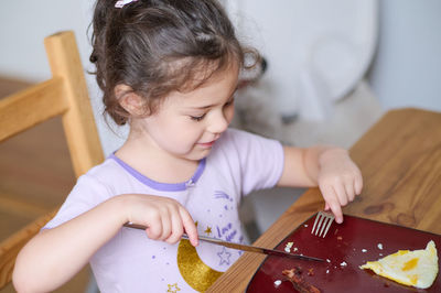 Young girl eating eggs and bacon with knife and fork for the first time