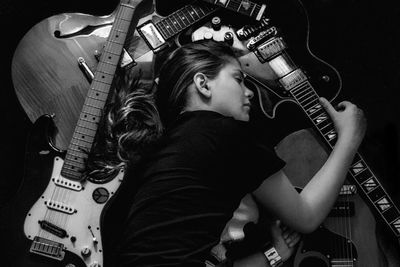 Young woman sleeping amidst guitar on black background