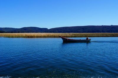 Man on boat sailing in river against clear blue sky