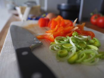 Close-up of wooden cutting board with sliced leek and paprika and a knife laying on it 