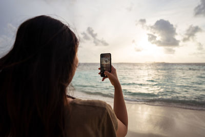 Rear view portrait of woman photographing sea against sky