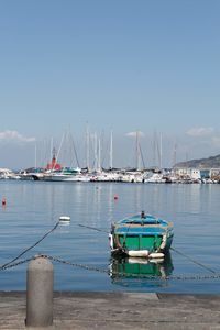 Sailboats moored at harbor against blue sky