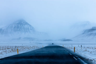 Road leading to snow covered mountain against sky with harsh winter conditions 