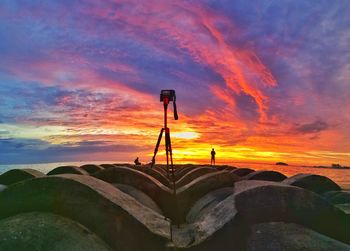 Tripod on rocks at beach against dramatic sky during sunset