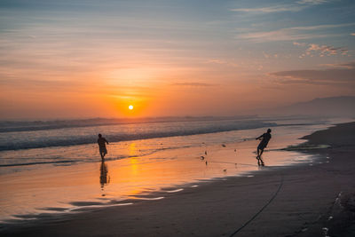 Silhouette people on beach against sky during sunset