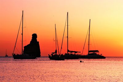 Silhouette sailboats sailing on sea against orange sky