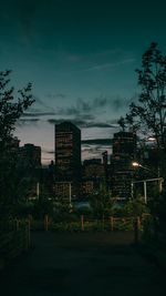 Illuminated street amidst buildings against sky at night