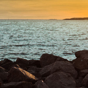 Close-up of rocks by sea against sky during sunset